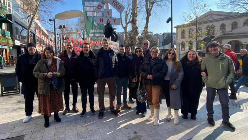 Partners of RISS project smiling in an urban area with a "Demir ve Yolu" sign and trees in the background