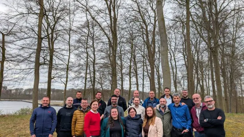 Group of professionals posing outdoors in a wooded area during overcast weather.