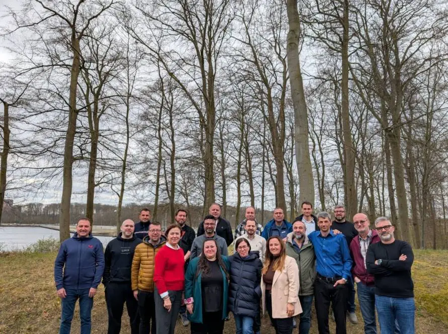 Group of professionals posing outdoors in a wooded area during overcast weather.