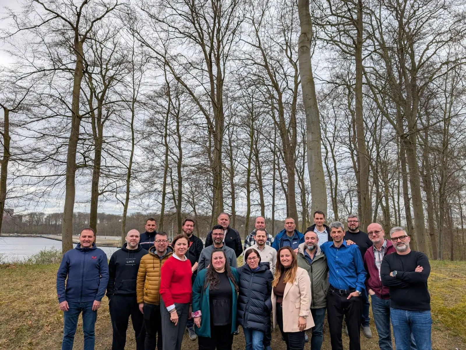 Group of professionals posing outdoors in a wooded area during overcast weather.