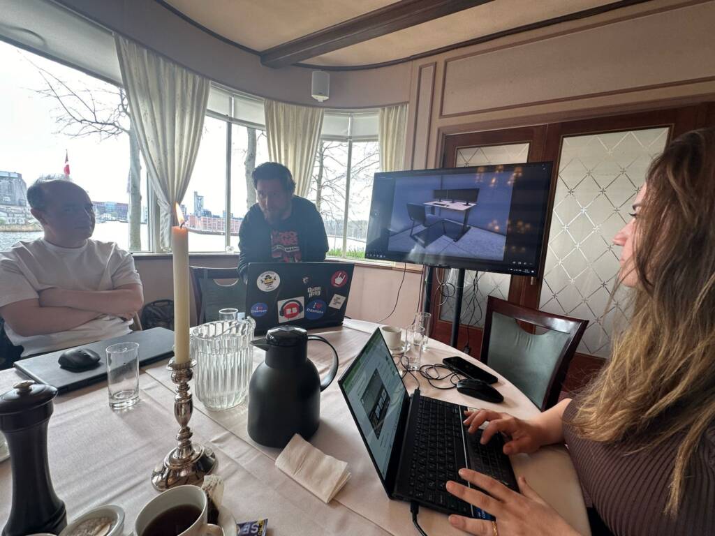 Colleagues discussing work inside a conference room with laptops and a presentation on a screen.